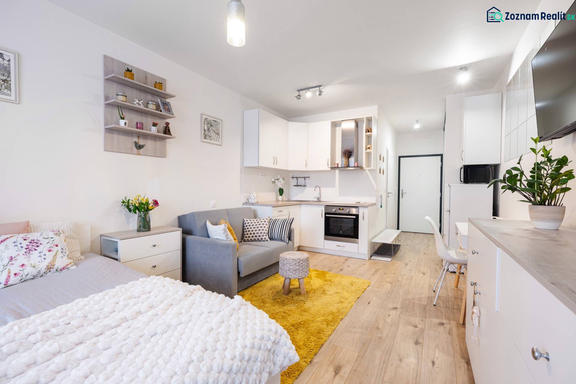 Světlý interiér 1-pokojového bytu s kuchyní, postelí a podlahou s dřevěným dekorem.