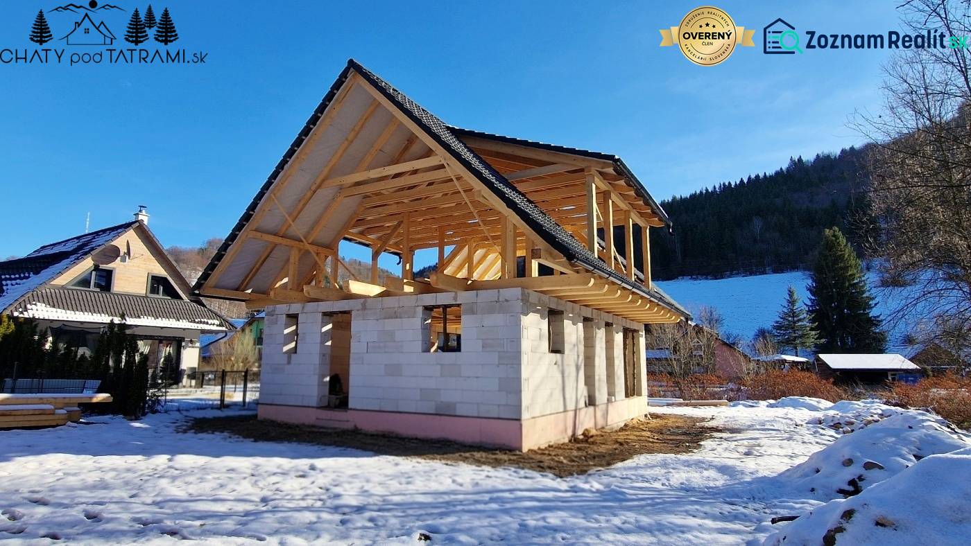 Stavba chaty na Mýtě pod Ďumbierem v zimní krajině s dřevěnou konstrukcí.