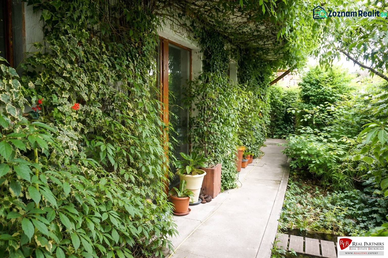 Zahrada 3pokojového bytu na Šancově ulici v Pezinku s bujnou zelení a chodníkem.