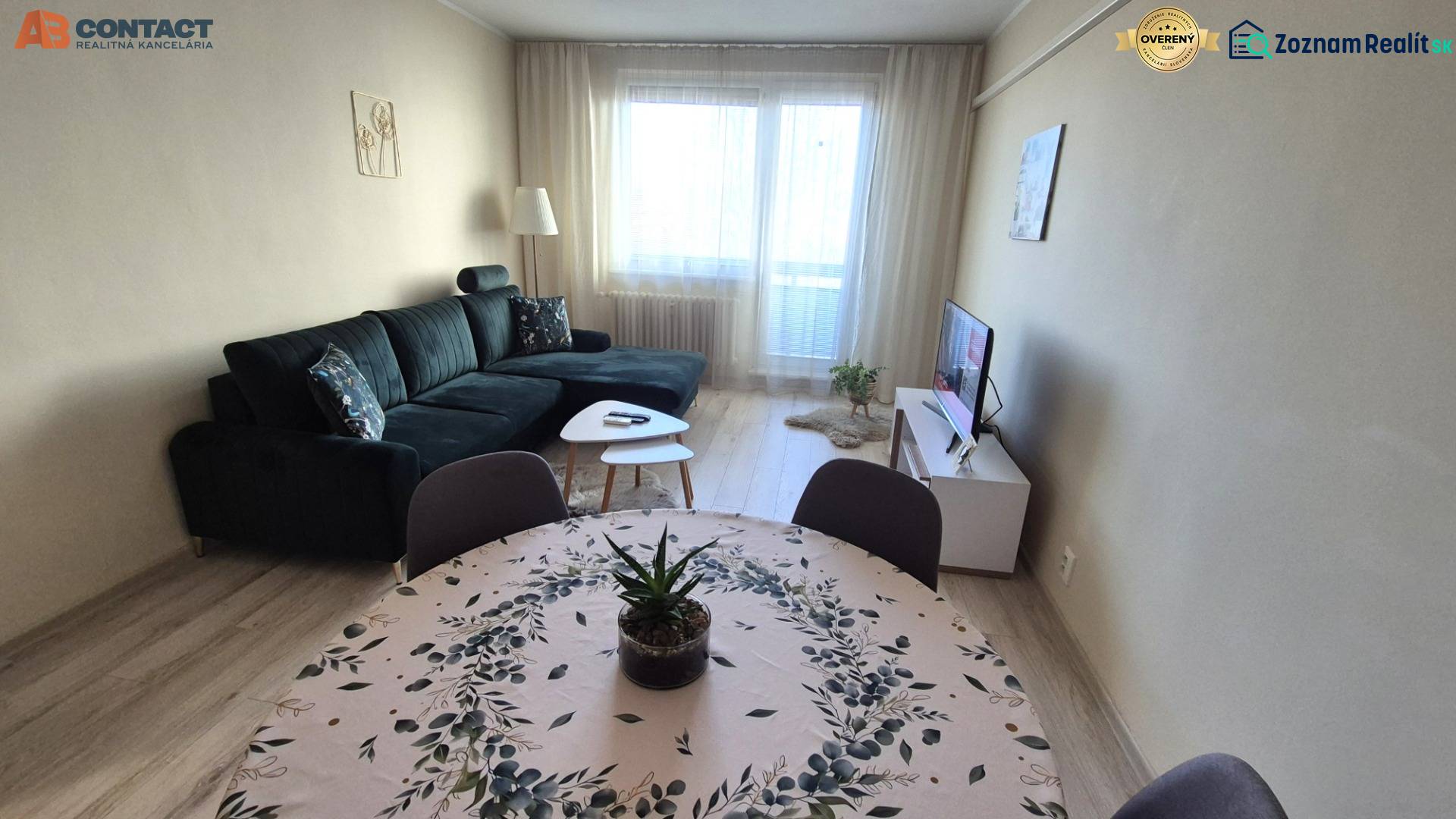 Obývací pokoj s tmavou sedačkou, jídelním stolem a podlahou s dřevěným dekorem v 2pokojovém bytě.