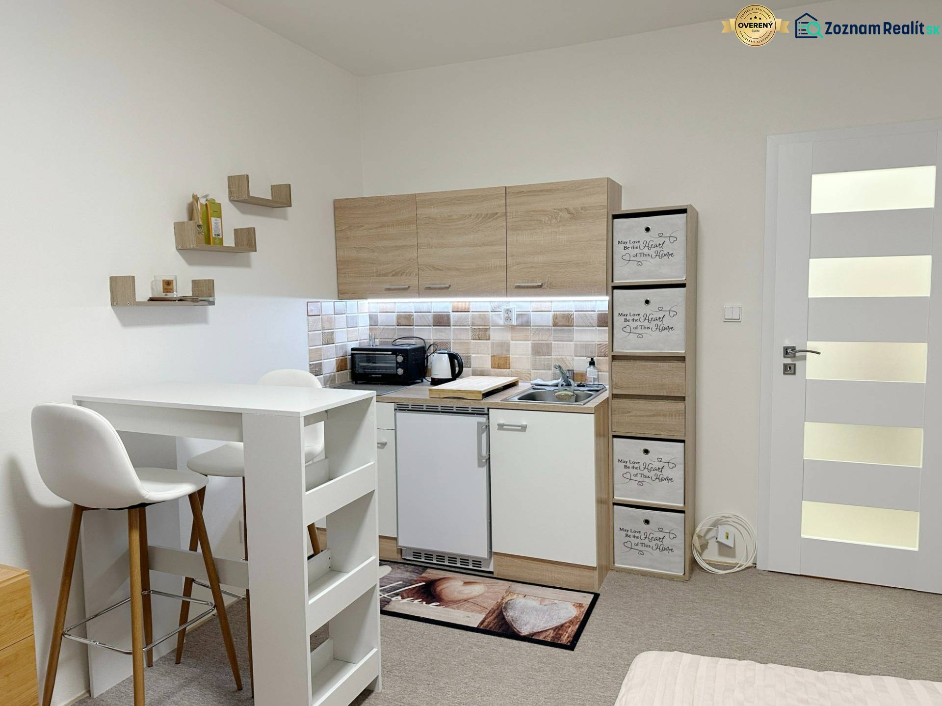 Garsonka s kuchyňkou, bílým stolem a židlemi, podlaha s dřevěným dekorem.