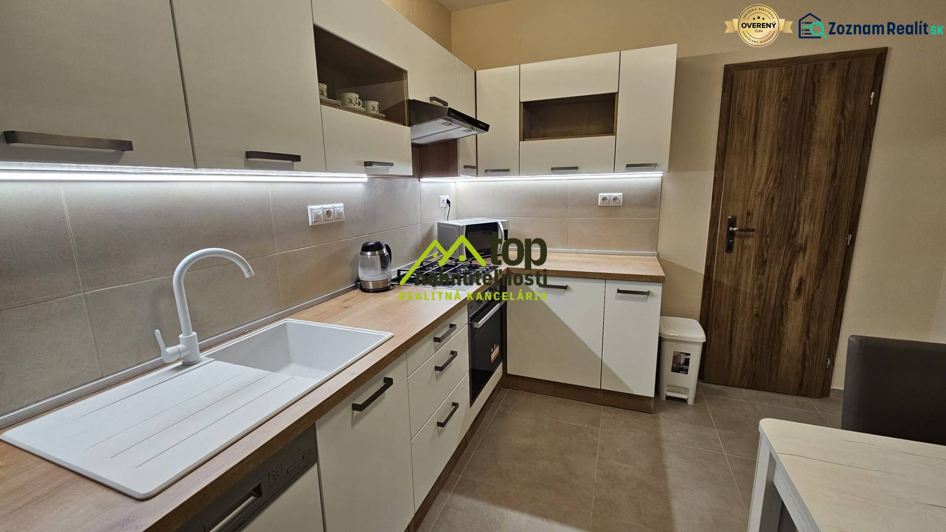 Kuchyně v 2-pokojovém bytě s bílými skříňkami a podlahou s dřevěným dekorem.