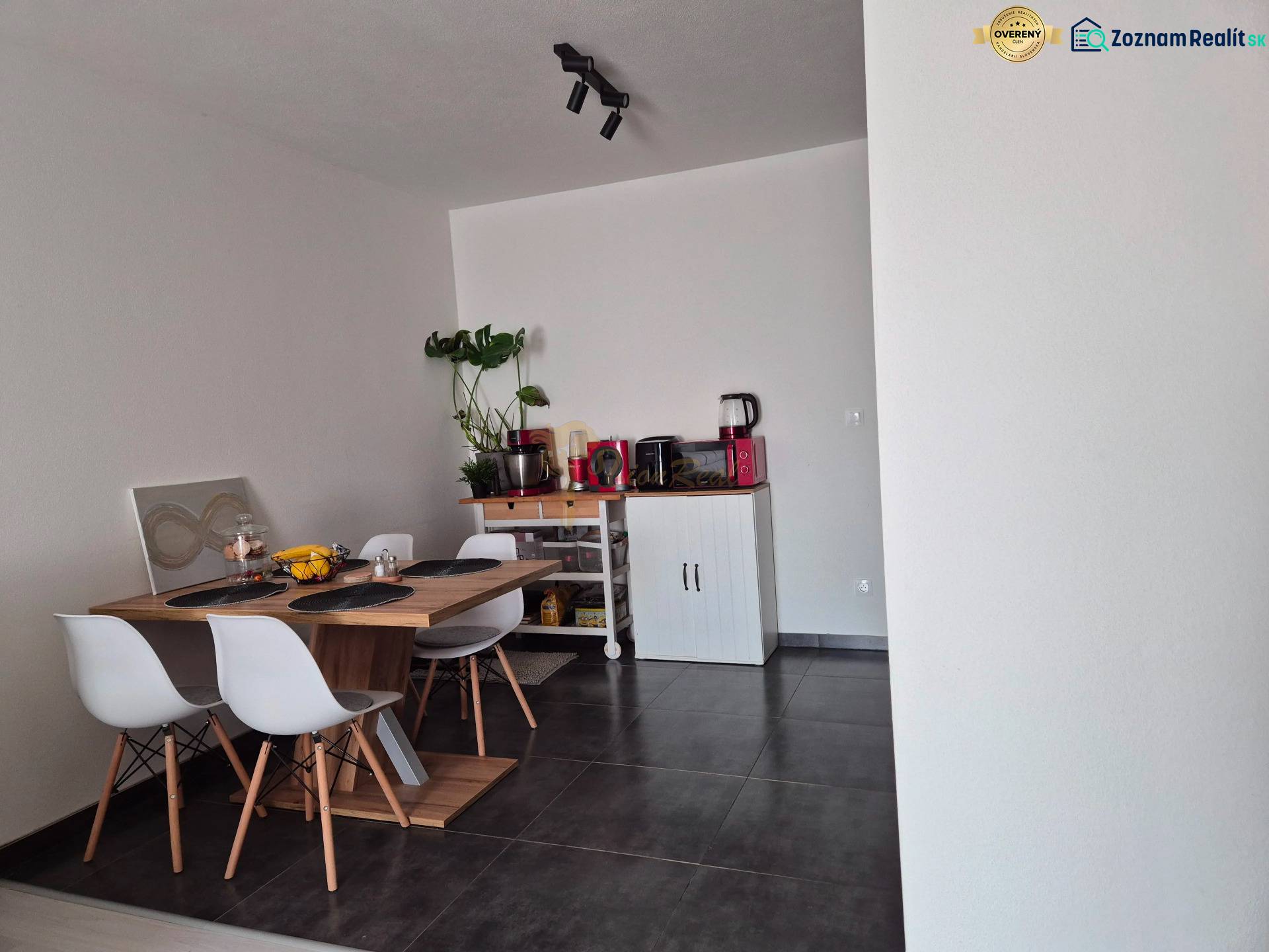 Jídelní kout s dřevěným stolem, čtyřmi židlemi a rostlinou v 3-pokojovém bytě.