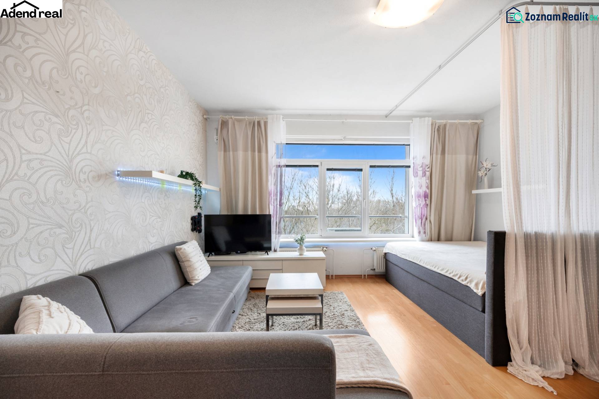 Obývací pokoj s pohovkou, závěsem a televizí, podlaha s dřevěným dekorem.