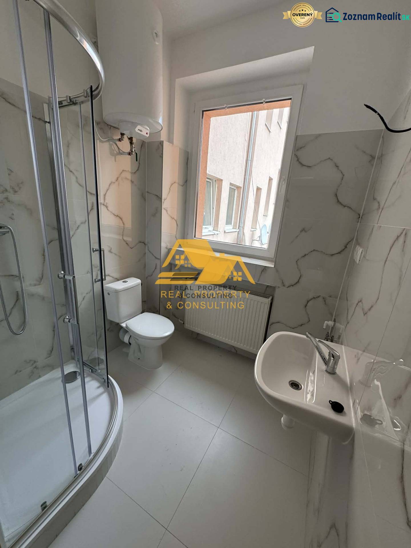 Koupelna v 1-pokojovém bytě s rohovým sprchovým koutem a keramickými obklady.