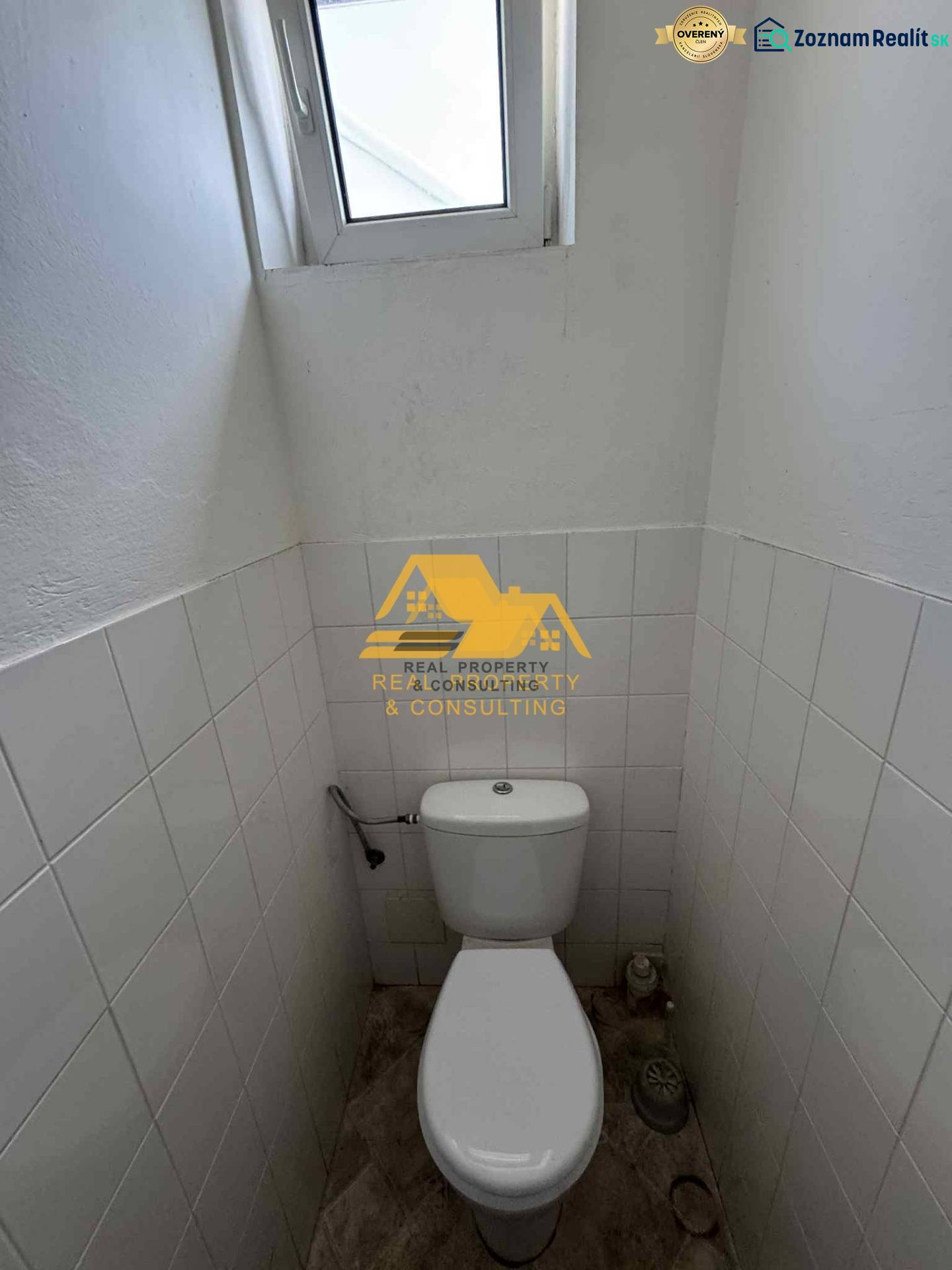 Kompaktní toaleta s oknem, bílé dlaždice, podlaha s dřevěným dekorem.