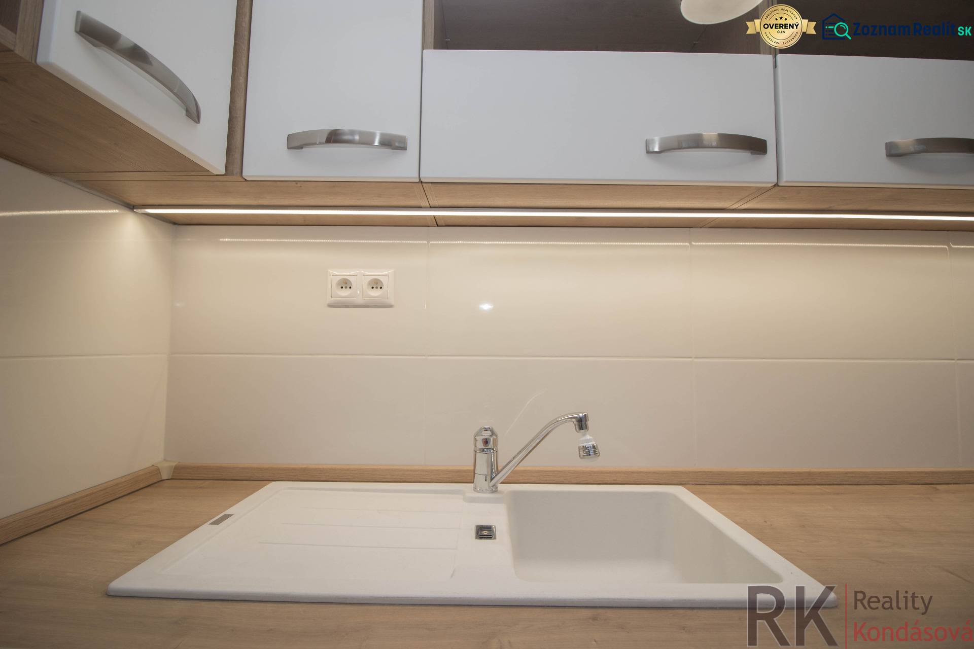 Kuchyňská pracovní deska s dřevěným dekorem a bílým dřezem v 2-pokojovém bytě.