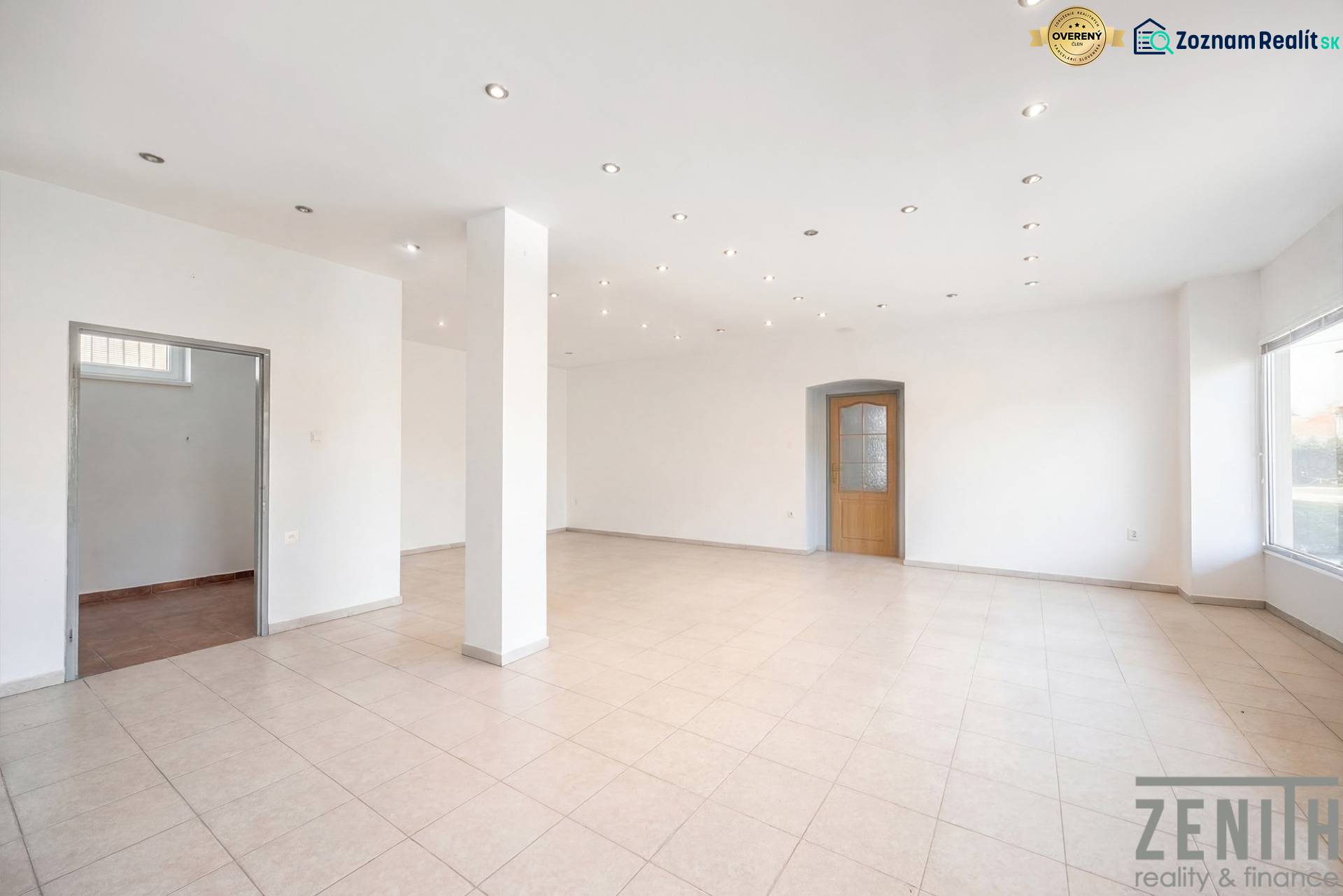 Prostorné obchodní prostory s bílými stěnami, dlažbou a rozsvícenými stropními světly.