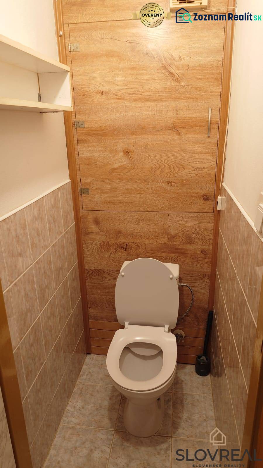 Toaleta se stěnami obloženými dlažbou a dveřmi s dřevěným dekorem v 2pokojovém bytě.