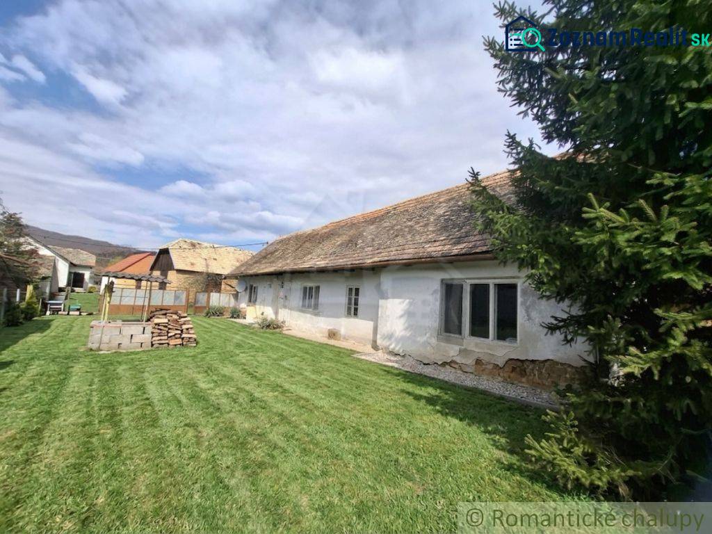 Rodinný dům v Ozdíně s původním vzhledem a travnatým dvorem, obklopený stromy.