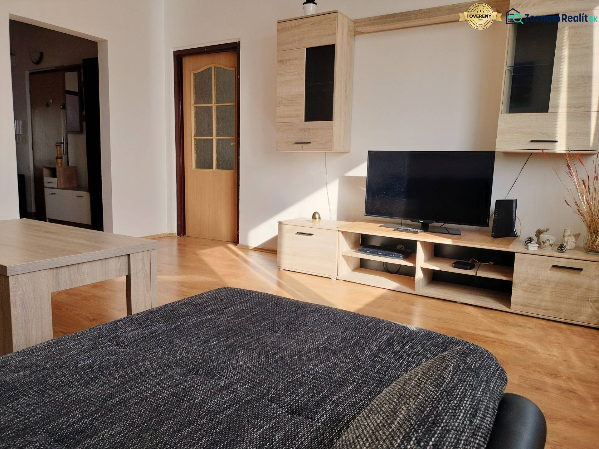 Obývací pokoj v 3-pokojovém bytě s podlahou s dřevěným dekorem, televizorem a nábytkem.