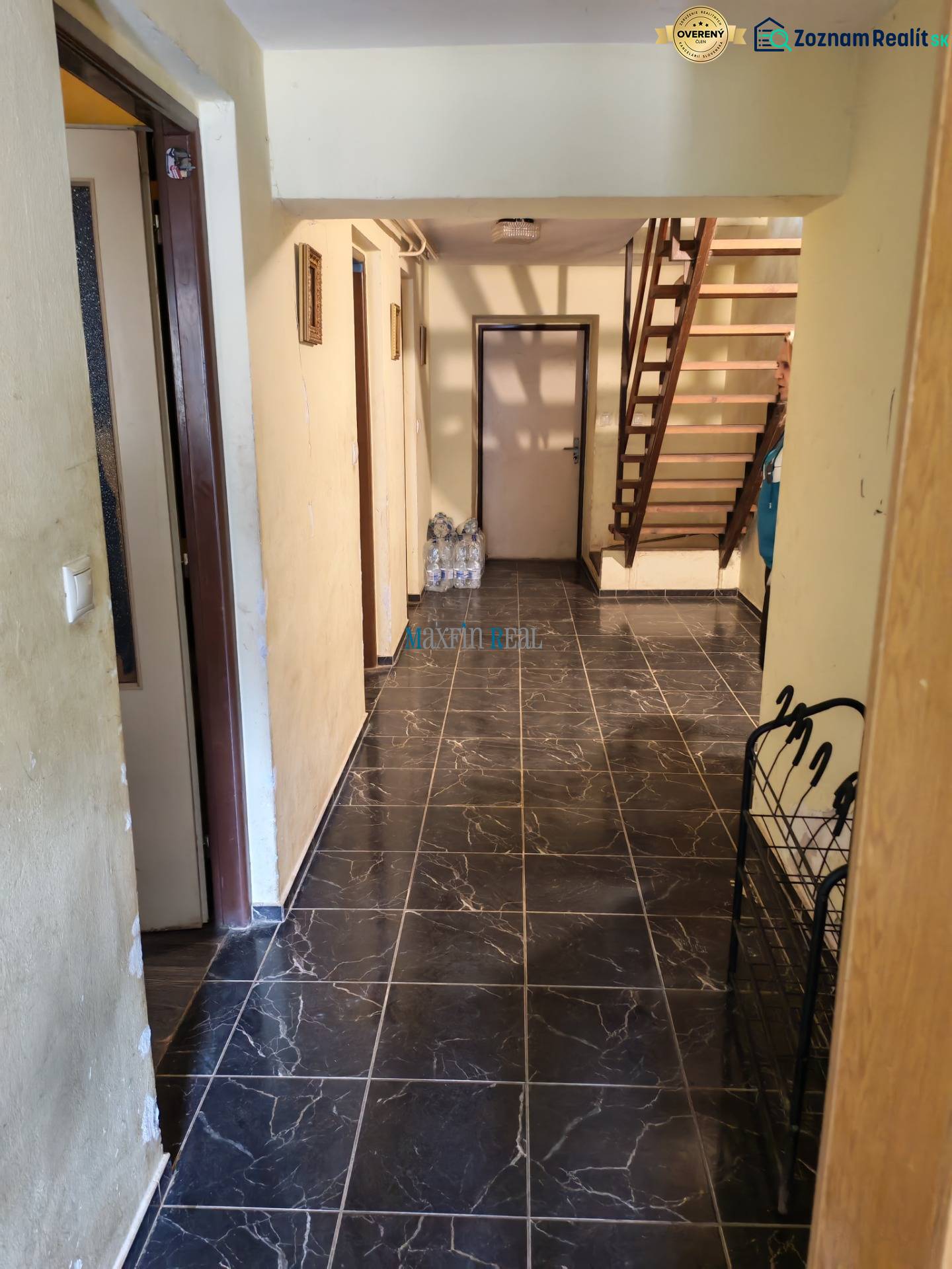 Interiér rodinného domu s tmavou dlažbou a dřevěným schodištěm.