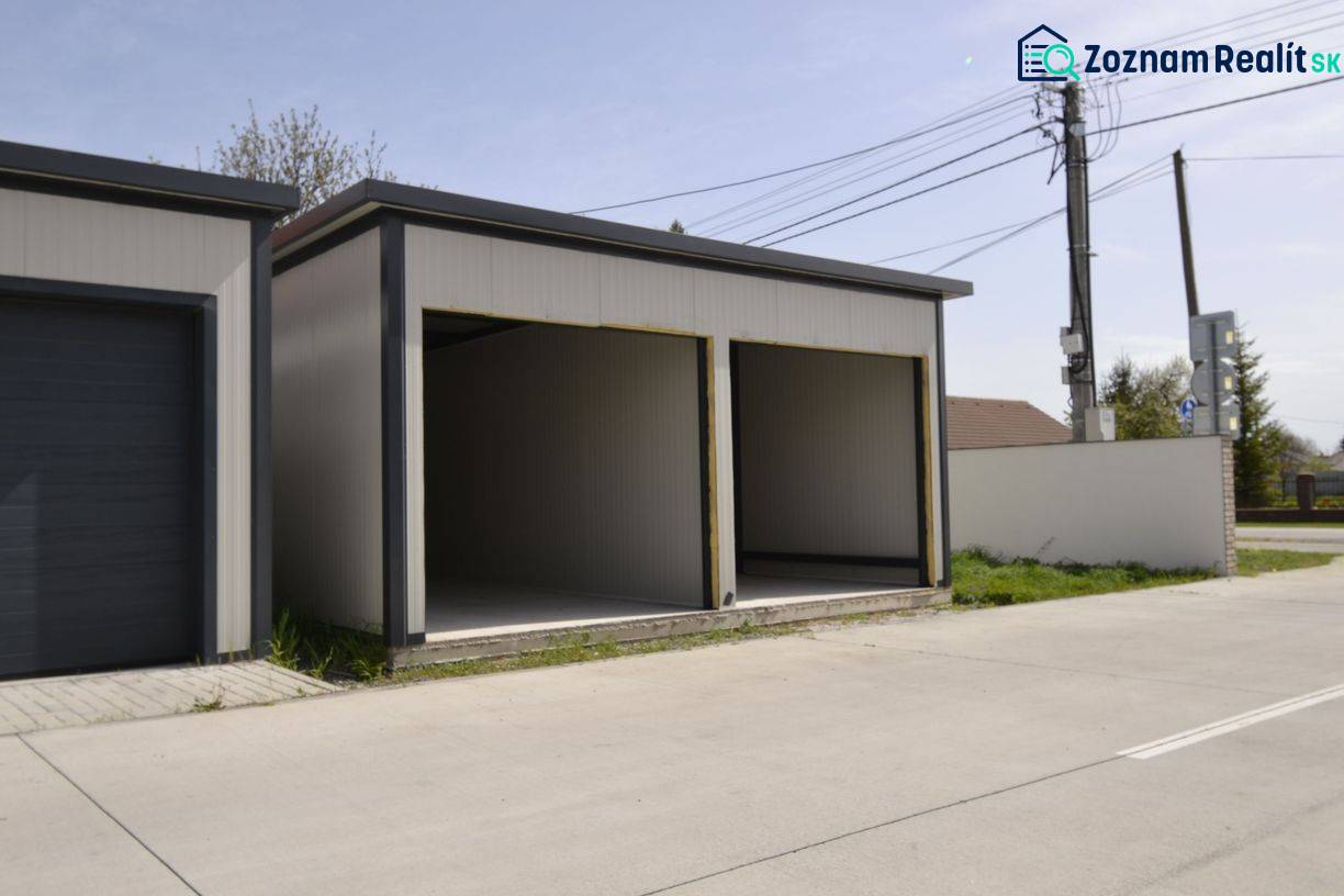 Garáže v Michali na Ostrově se dvěma otevřenými vjezdy, vedle cesty a plotu.