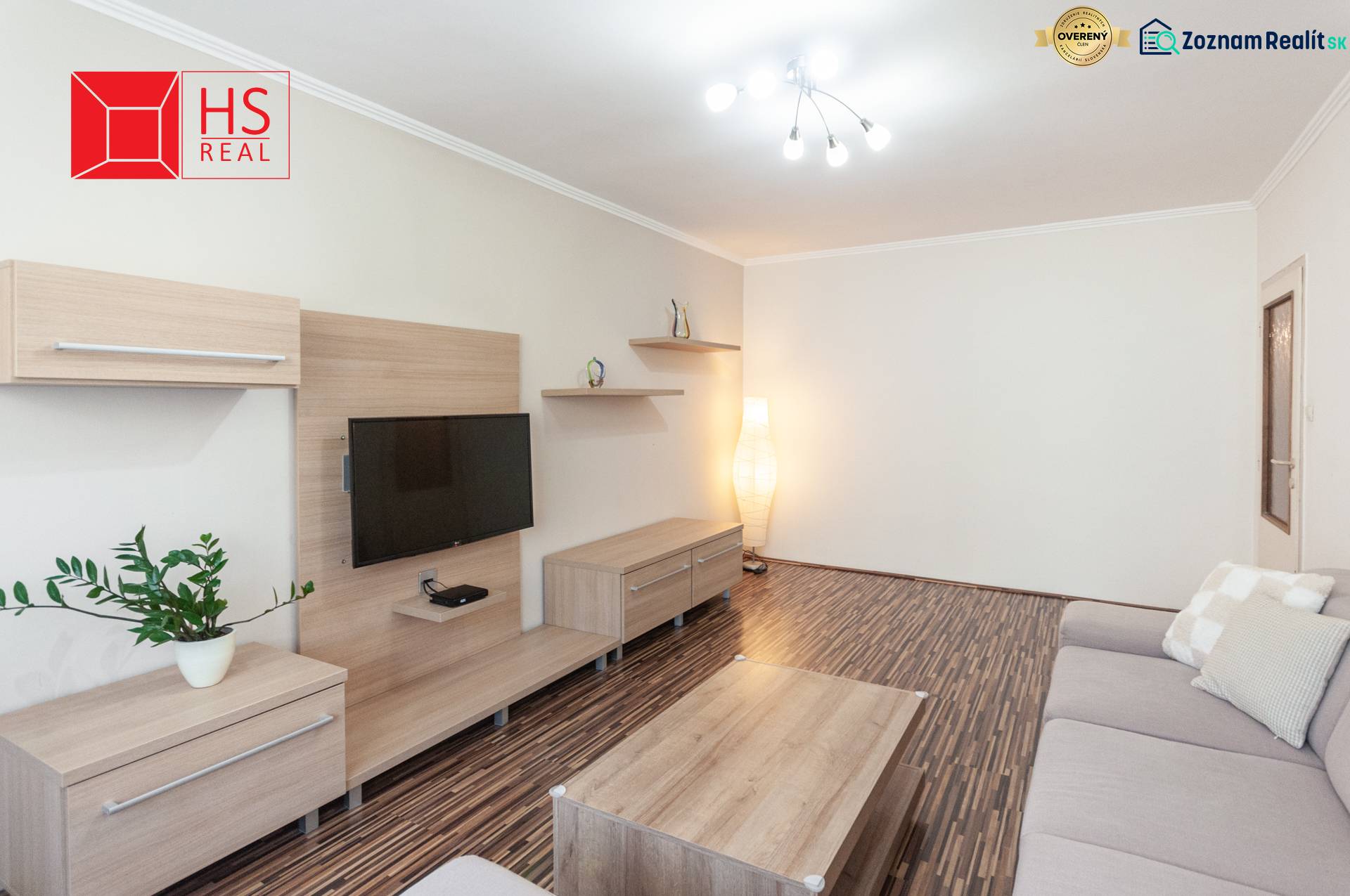 Obývací pokoj třípokojového bytu s podlahou s dřevěným dekorem a šedou pohovkou.