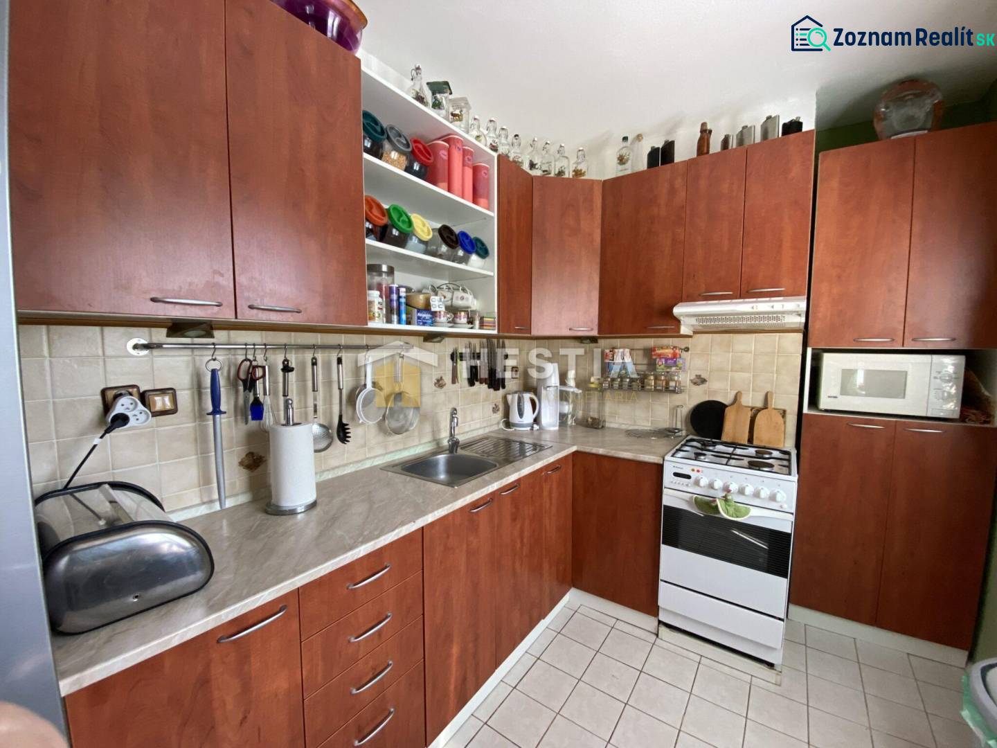 Kuchyně v 2-pokojovém bytě s dřevěnými skříňkami a bílou dlažbou.