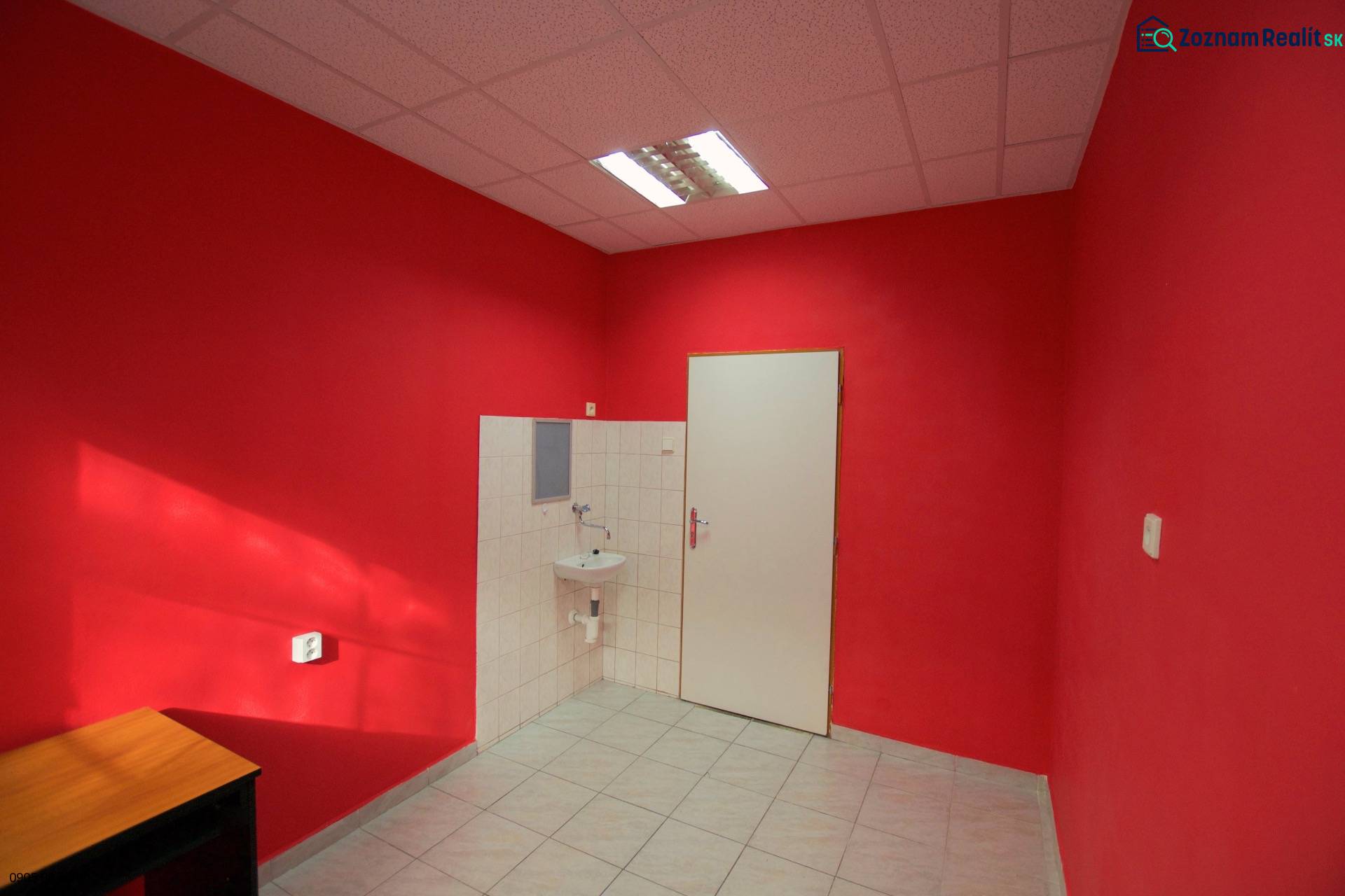 Interiér obchodního prostoru s červenými stěnami, umyvadlem a bílými dlaždicemi.
