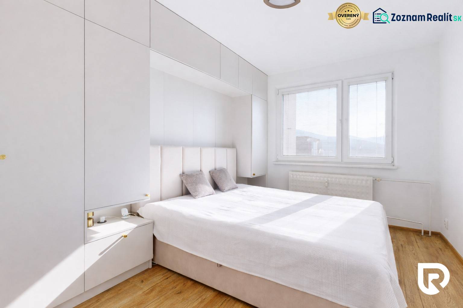 Ložnice v 3-pokojovém bytě s podlahou s dřevěným dekorem, bílý nábytek a velké okno.