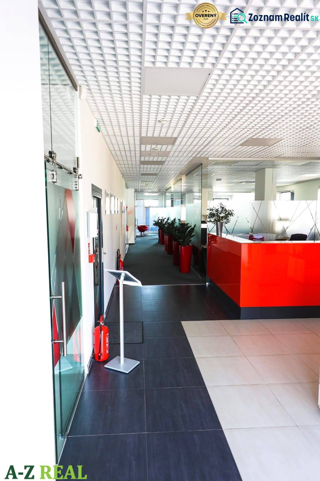 Chodba v kancelářích s červenou recepcí, rostliny v červených květináčích.