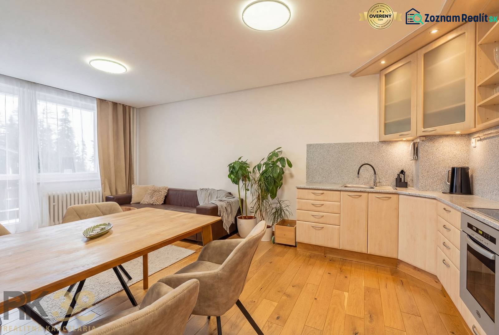 Interiér rekreačního apartmánu s pohovkou, kuchyní a podlahou s dřevěným dekorem.