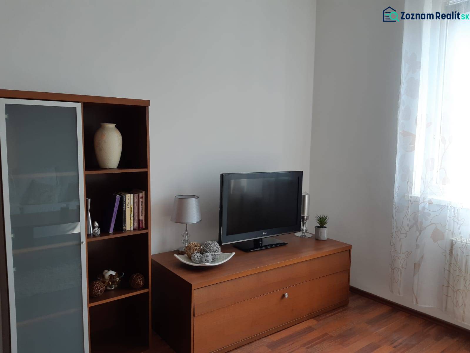 Obývací pokoj s podlahou s dřevěným dekorem, knihovnou, televizorem a dekorativními předměty.