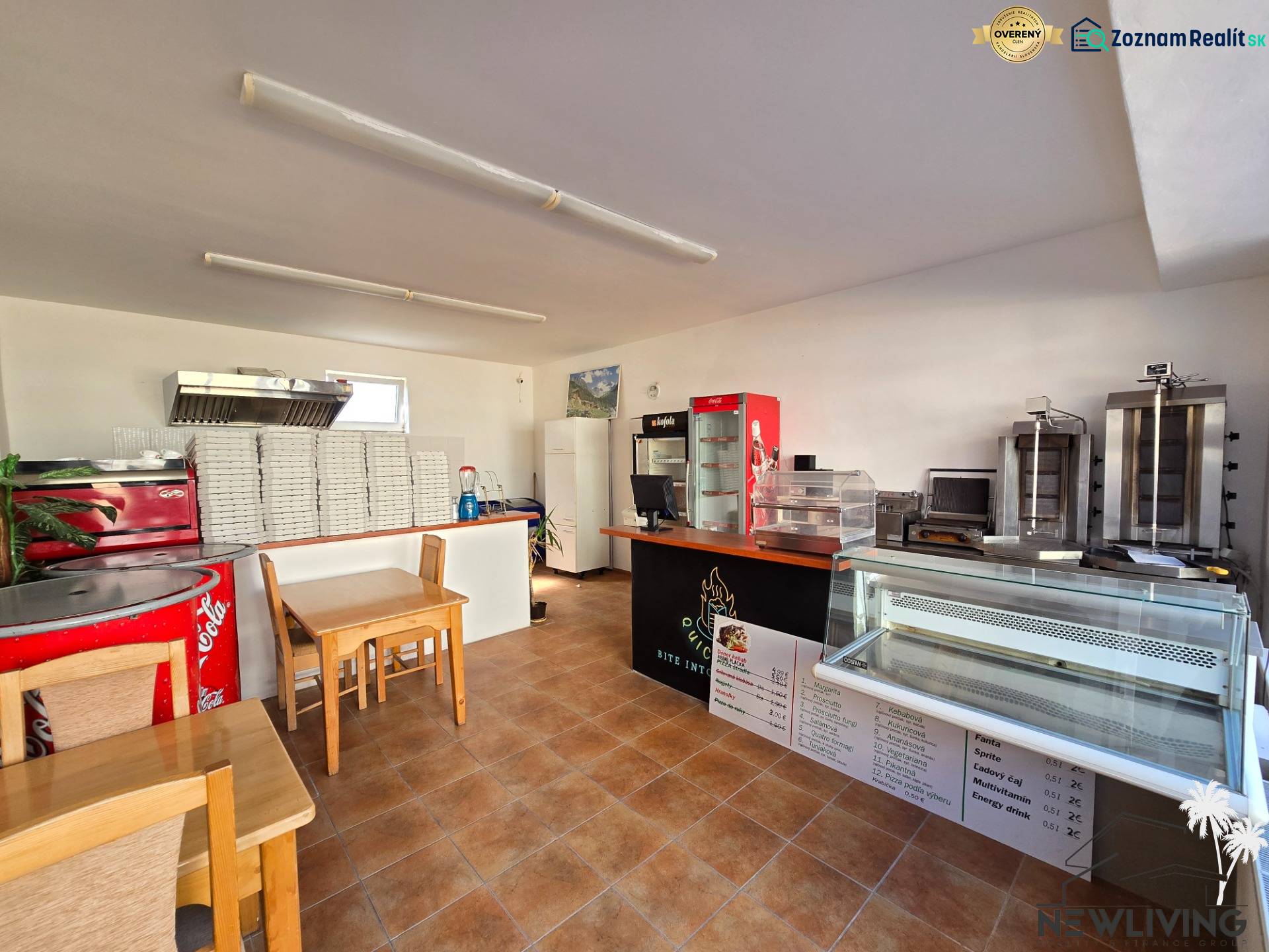 Interiér gastro prostor s pultem, chladicími vitrínami a stoh krabic na pizzu.
