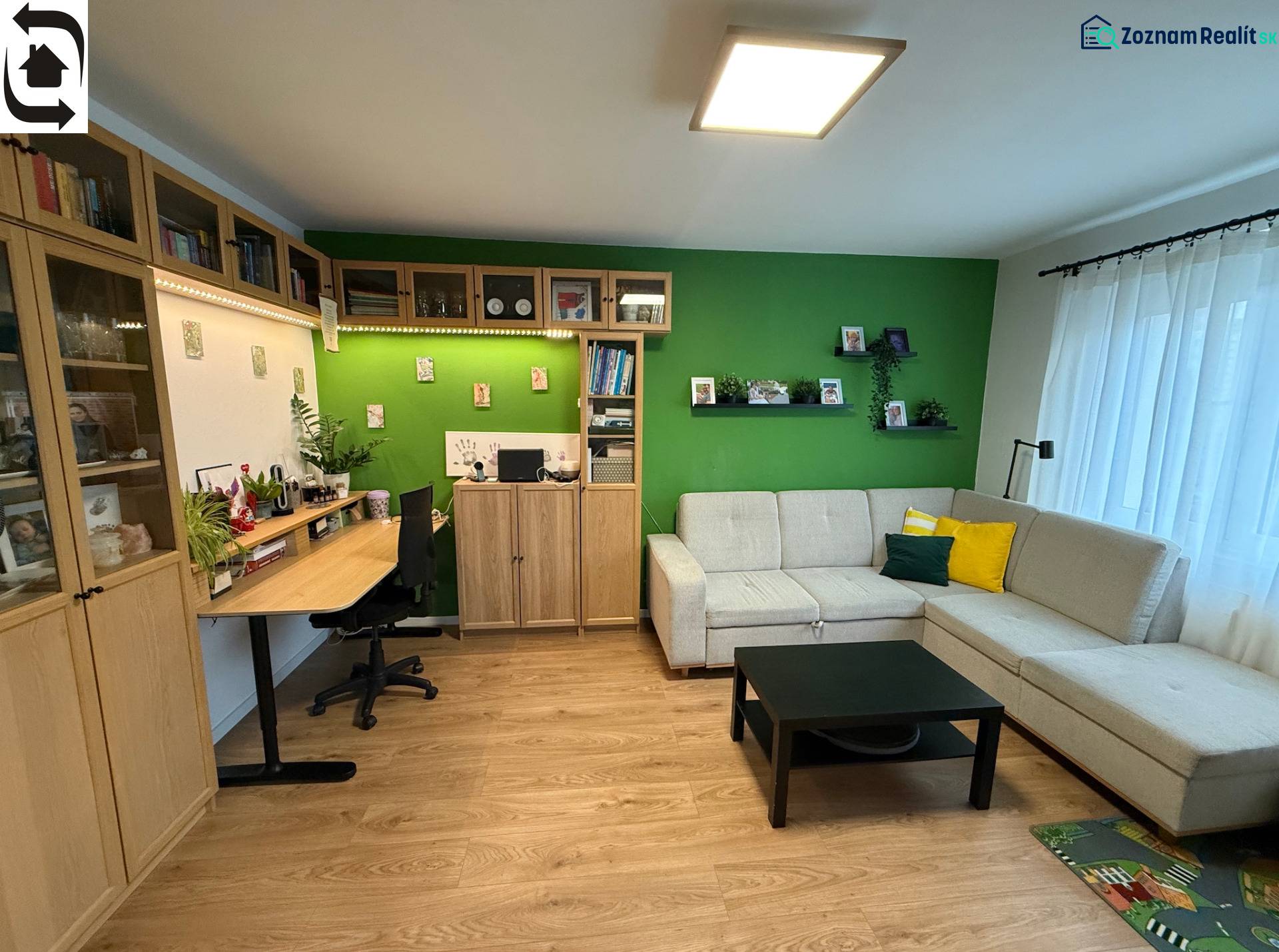 Obývací pokoj s pohovkou, pracovním stolem a podlahou s dřevěným dekorem ve 4pokojovém bytě.