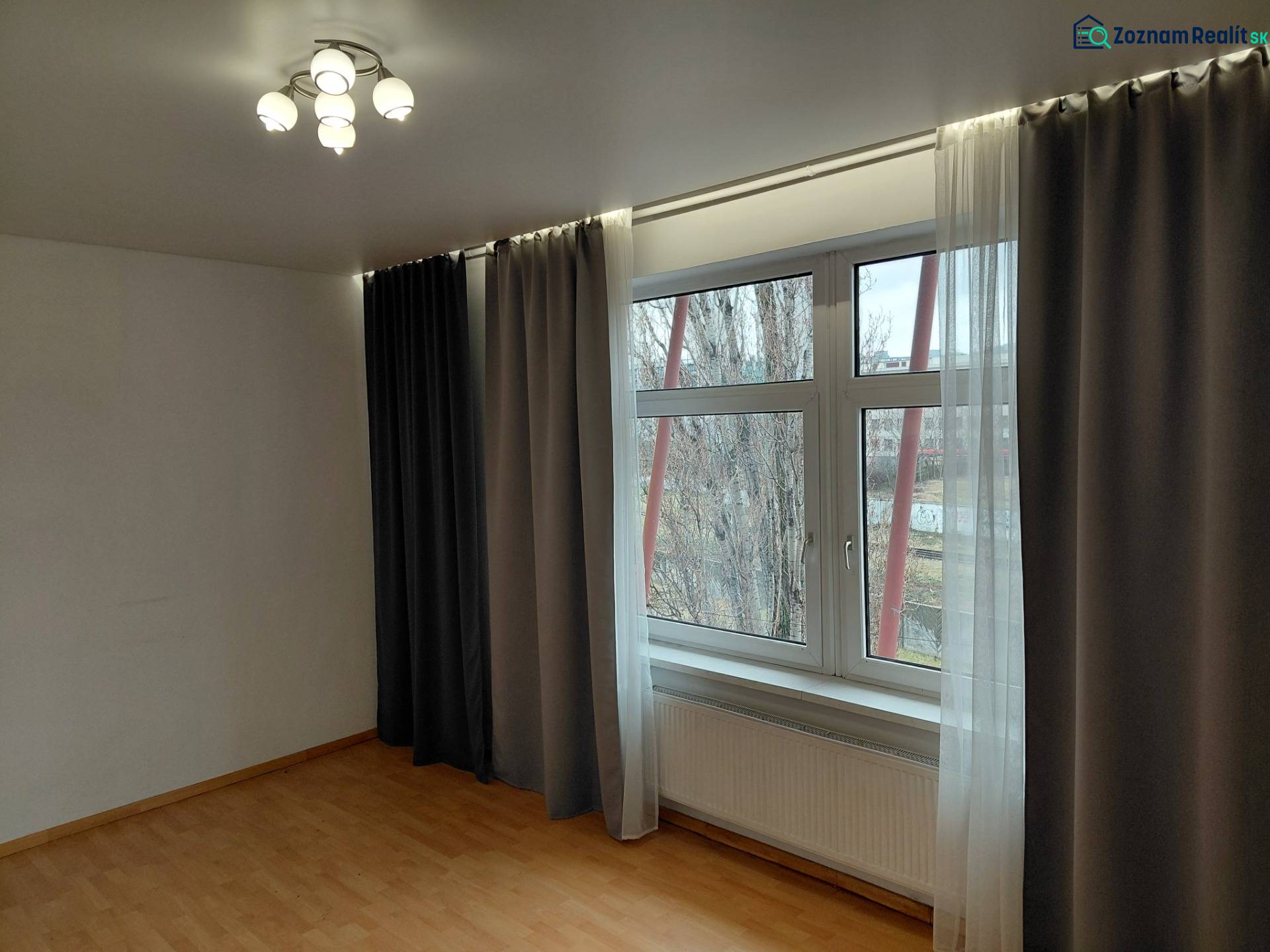 Pokoj s velkým oknem, zatemňovacími závěsy a podlahou s dřevěným dekorem. Obchodní prostory.