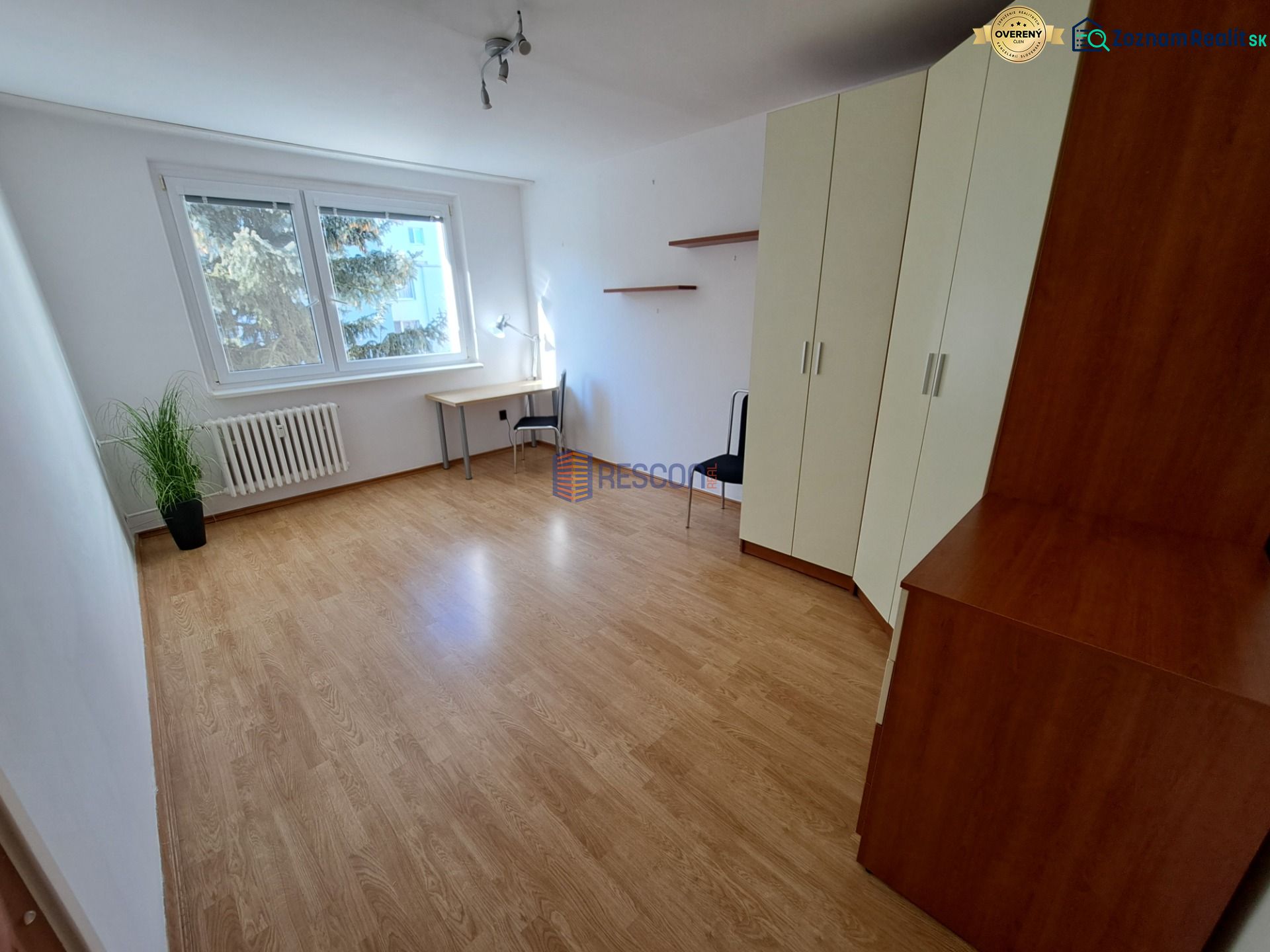 Pokoj s podlahou s dřevěným dekorem, velkými okny, skříní a psacím stolem.
