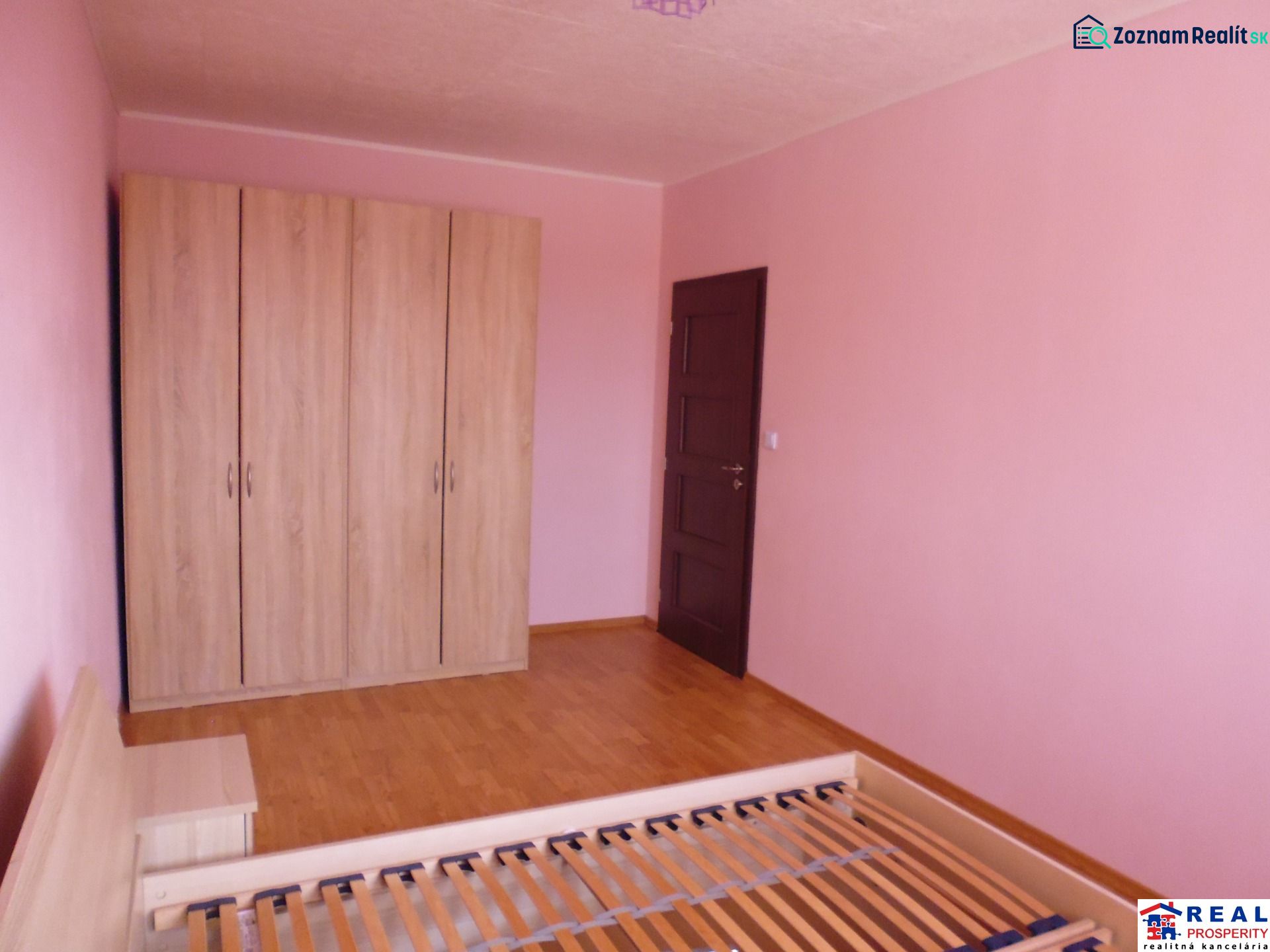 Pokoj v 2-pokojovém bytě s růžovými stěnami, skříní a podlahou s dřevěným dekorem.