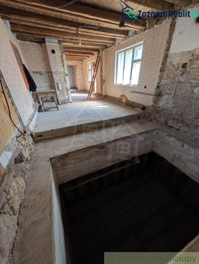Interiér rodinného domu s odkrytým stropem a surovými stěnami v rekonstrukci.