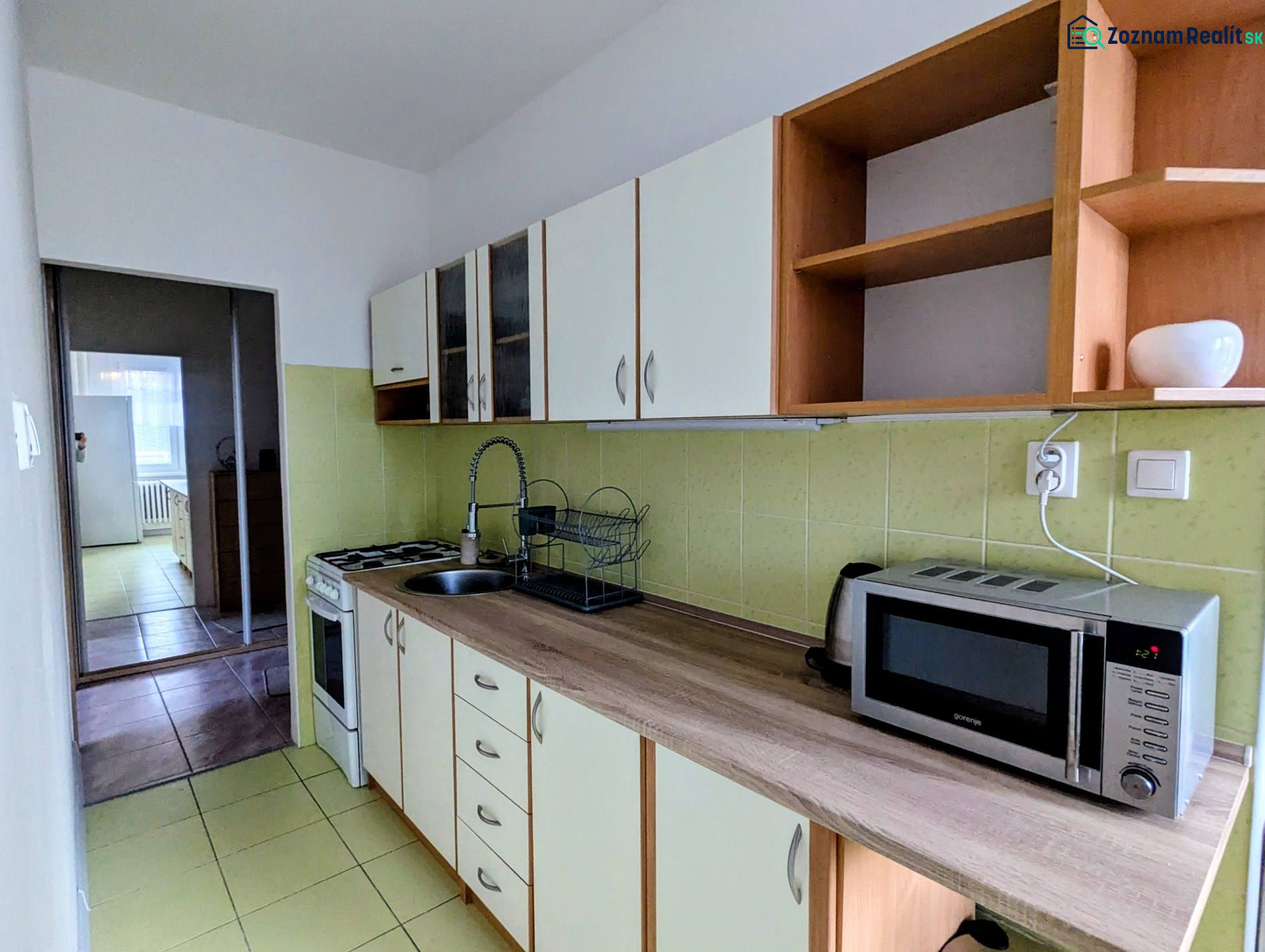 Kuchyně v 2-pokojovém bytě s mikrovlnkou a varnou deskou, směřující do další místnosti.
