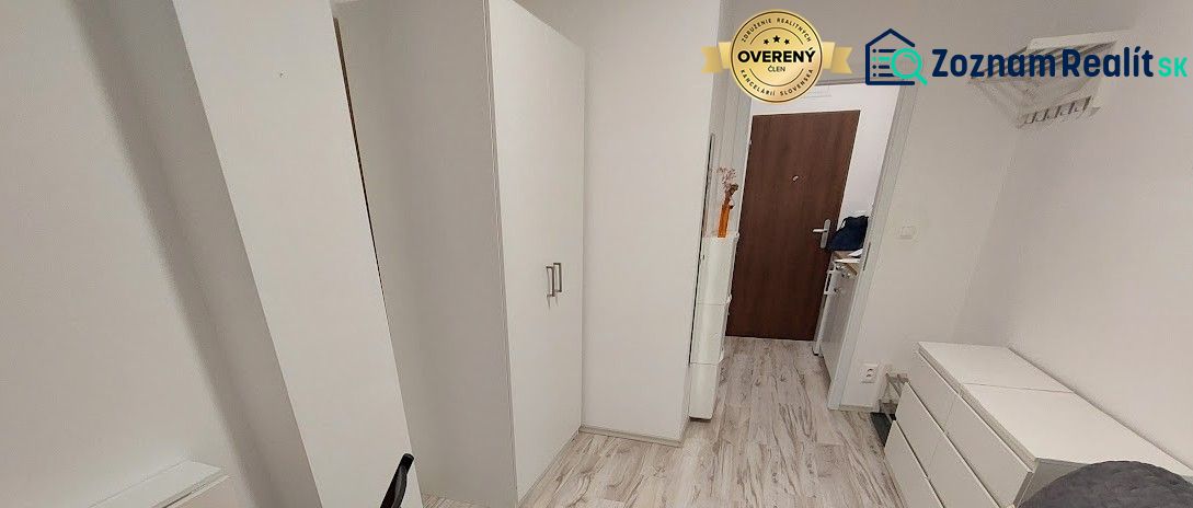 Útulná garsonka s bílým nábytkem a podlahou s dřevěným dekorem.