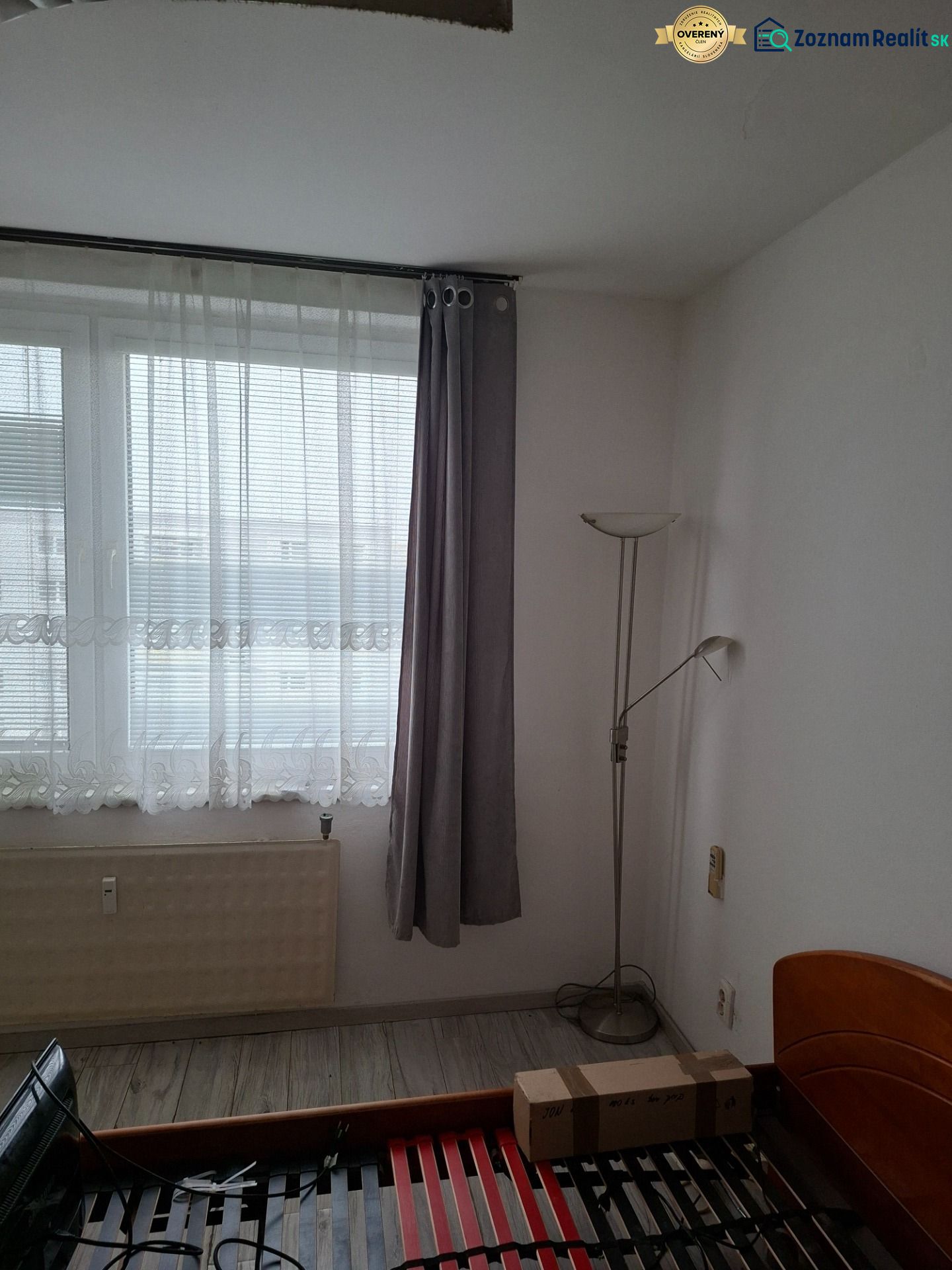Pokoj s postelí, okny a podlahou s dřevěným dekorem ve 2pokojovém bytě.