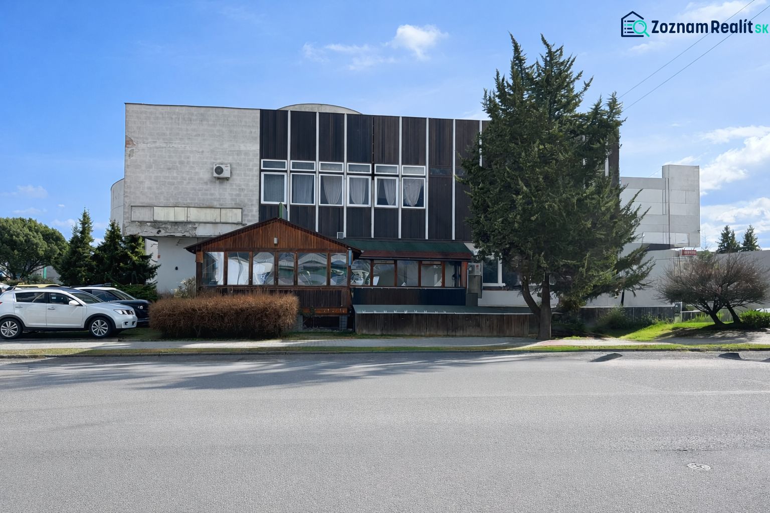 Exteriér gastro prostorů v Žiaru nad Hronom, obklopený stromy a zaparkovanými auty.