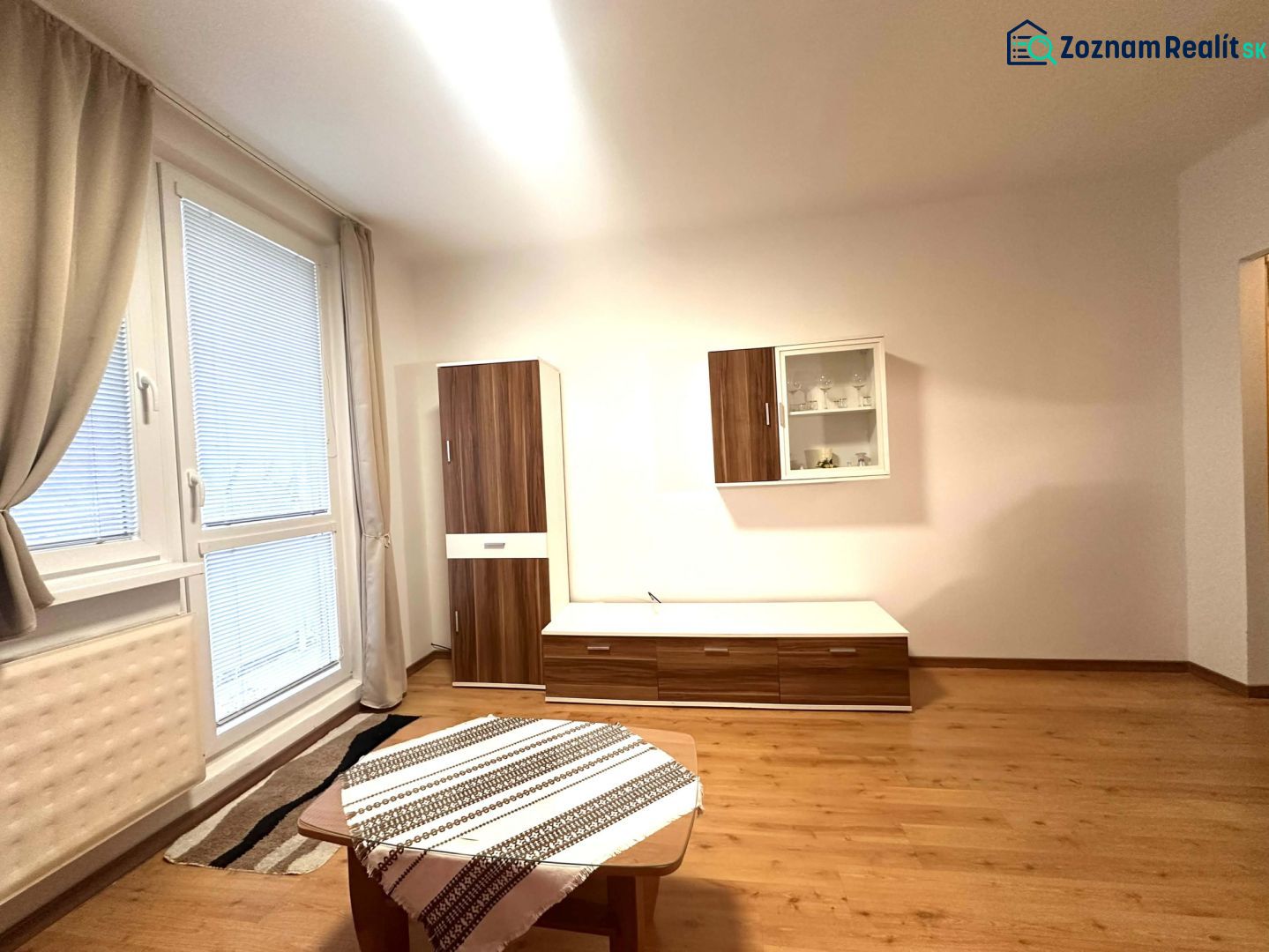 Rekreační apartmán s podlahou s dřevěným dekorem, nábytkem a velkým oknem.