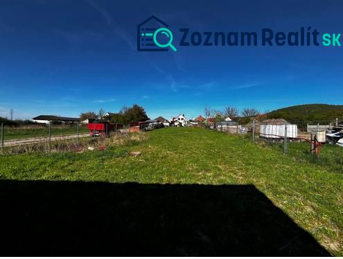 Pozemky - bydlení v Perneku, otevřená zelená plocha, s oplocením a venkovskou scénou v pozadí.