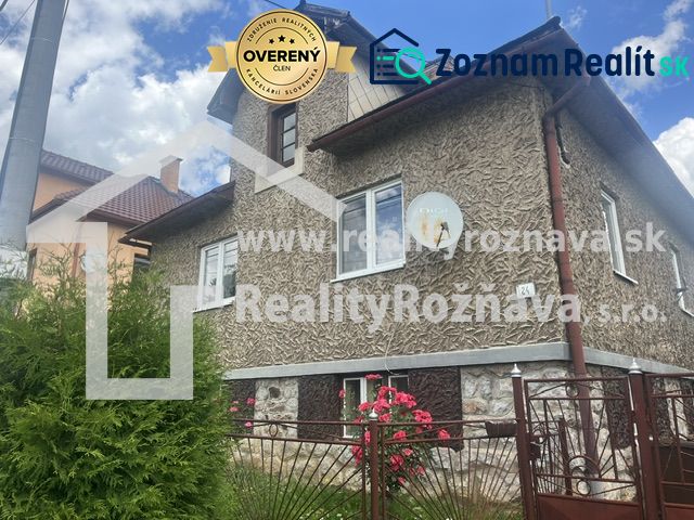 Rodinný dům v Rudné s texturovanou fasádou, zeleným plotem a květinami v zahradě.