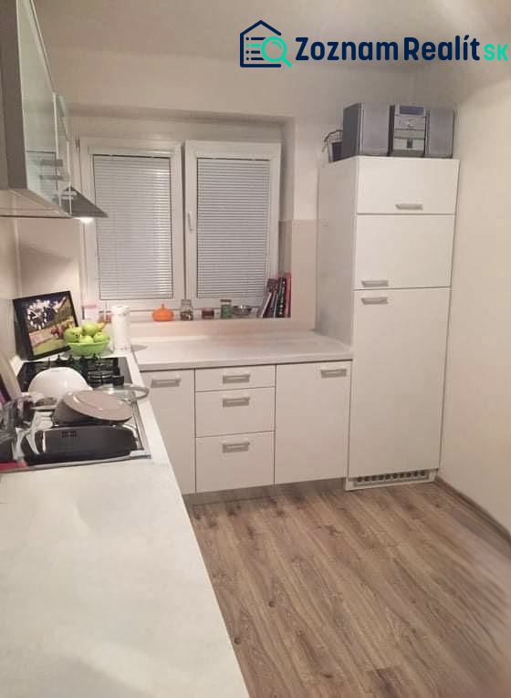 Kuchyně v 2-pokojovém bytě s bílými skříňkami a podlahou s dřevěným dekorem.