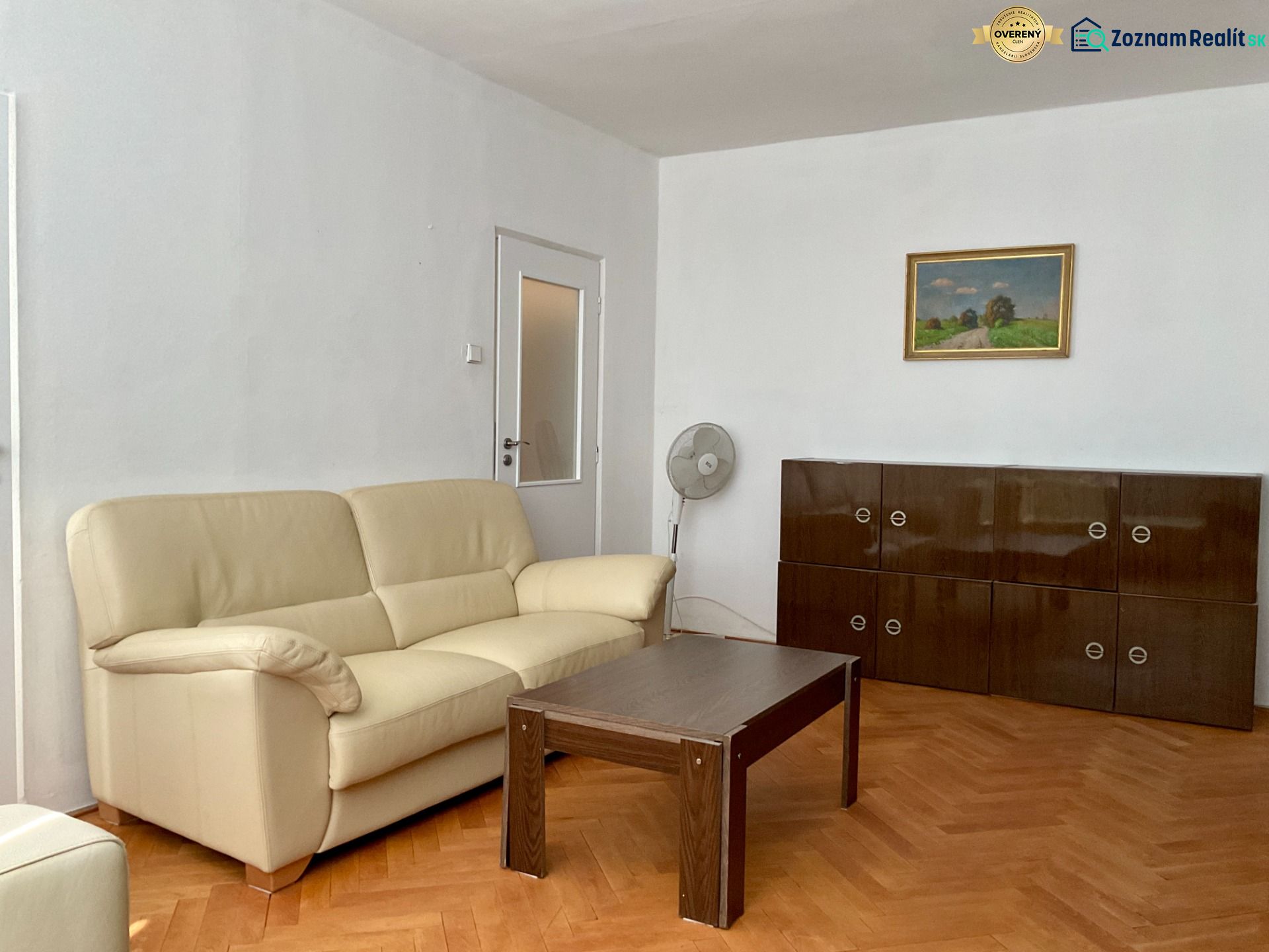 Obývací pokoj s krémovou sedačkou, dřevěným stolkem a skříňkou na podlaze s dřevěným dekorem.