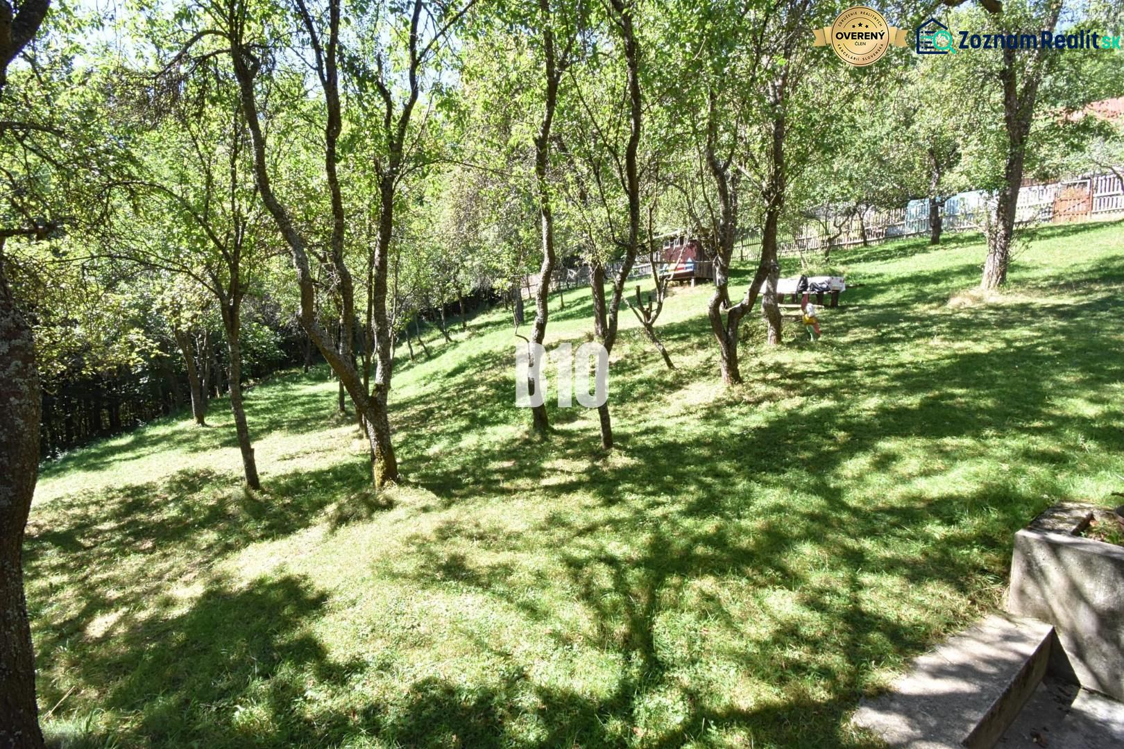 Zahrada v Dlouhém Poli u rodinného domu s travnatou plochou a stromy.