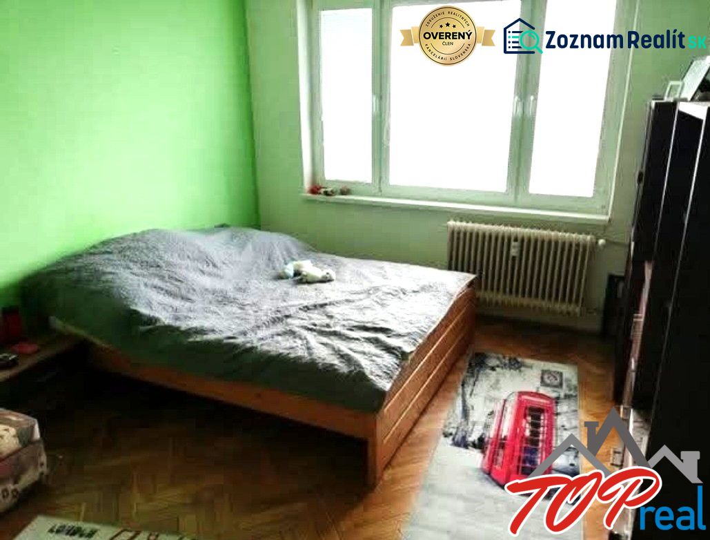 Ložnice v jednopokojovém bytě se zelenou stěnou a podlahou s dřevěným dekorem.