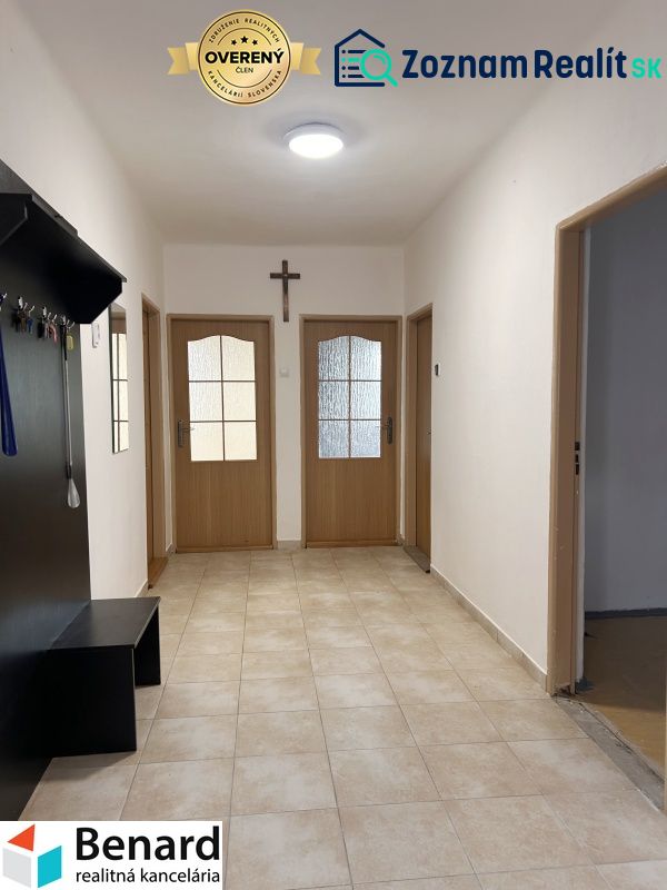 Chodba v rodinném domě s dlažbou, dřevěnými dveřmi a věšákem.