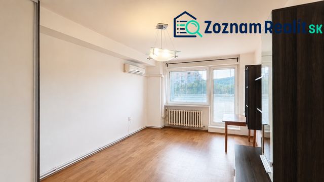 Obývací pokoj s podlahou s dřevěným dekorem, klimatizací a velkým oknem ve 3pokojovém bytě.