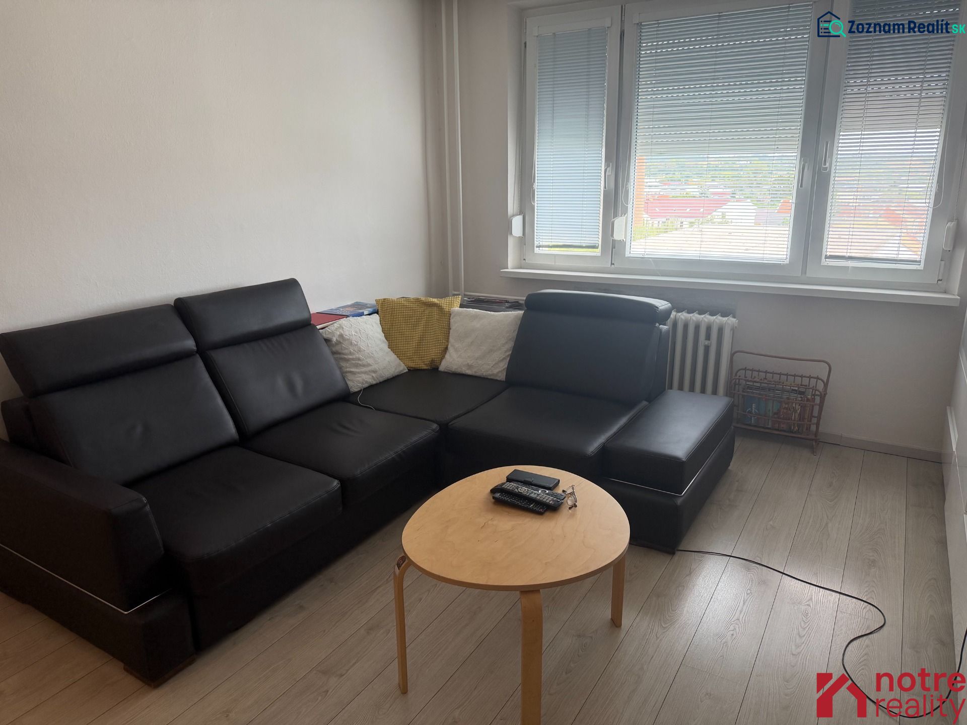 Obývací pokoj v 2pokojovém bytě s černou pohovkou a podlahou s dřevěným dekorem.