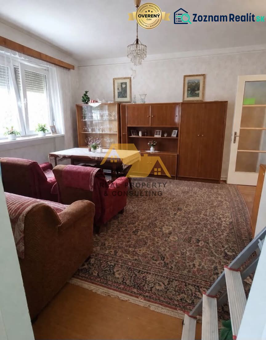 Obývací pokoj v rodinném domě s sedací soupravou, skříňkou a lustrem, podlaha s dřevěným dekorem.