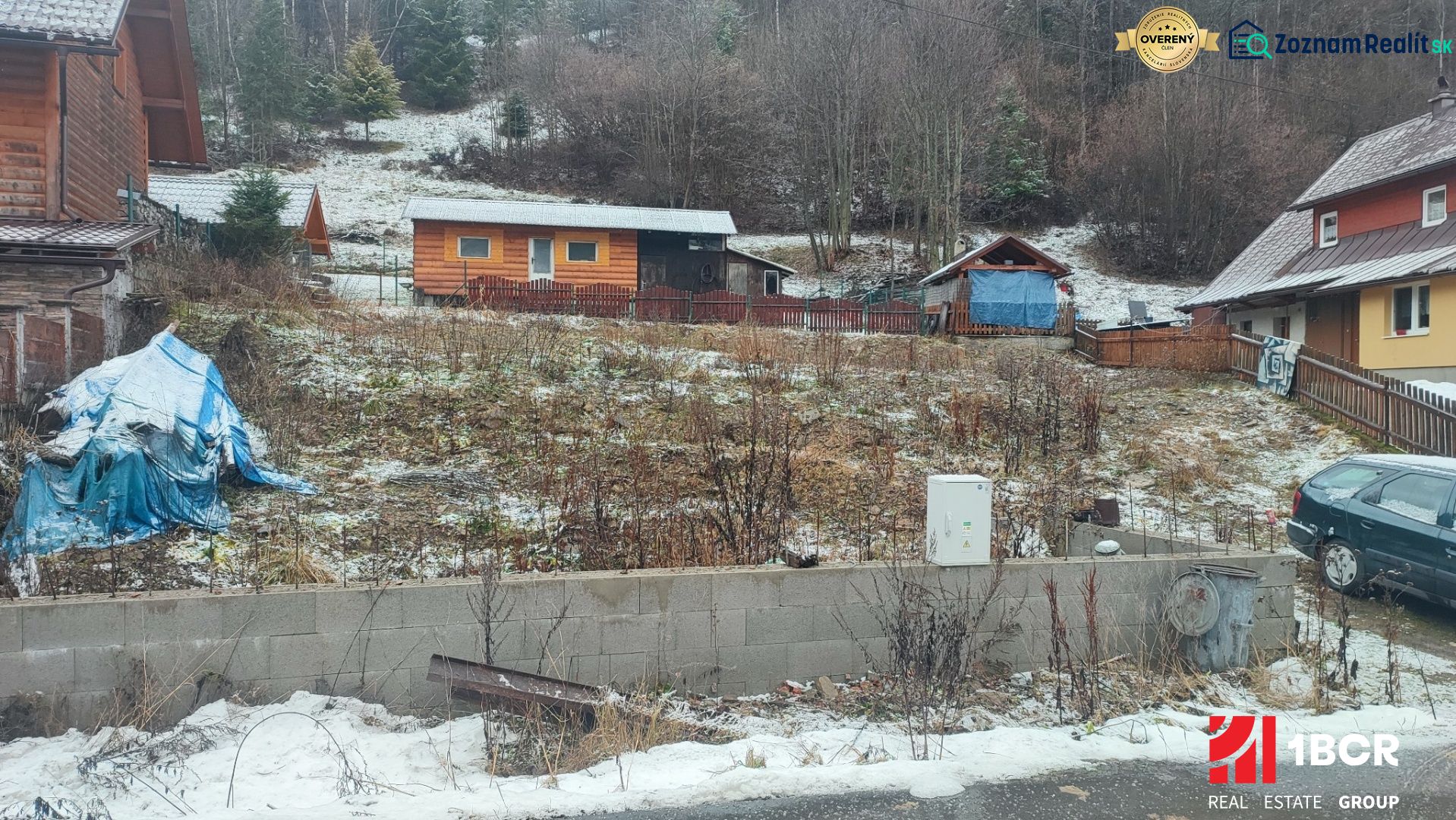 Sněhem pokrytý pozemek s rodinným domem v Oščadnici obklopený zelení a dřevěnými strukturami.