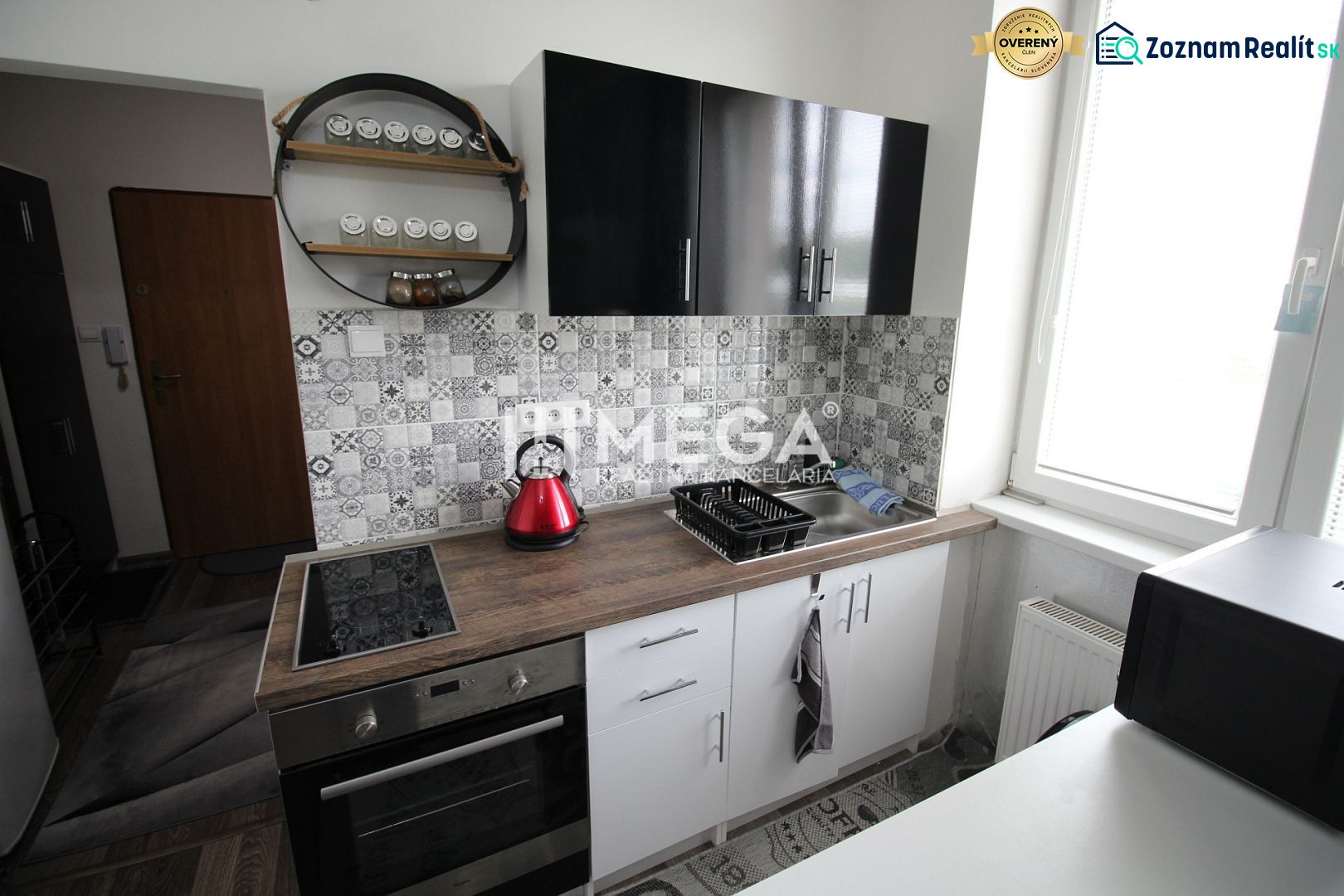 Kuchyně rekreačního apartmánu s černými skříňkami, varnou deskou a dekorativním obkladem.