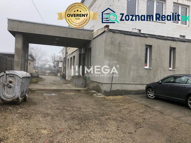 Budova na ulici SNP v Snině se zaparkovaným autem a kontejnerem na štěrkovém povrchu.