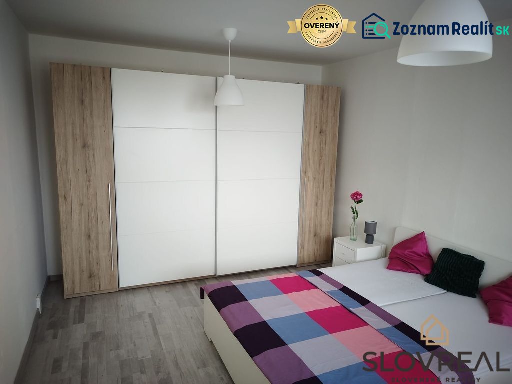 Ložnice s podlahou s dřevěným dekorem v 1+kk bytě, šatní skříň a postel.