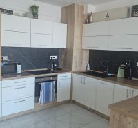 Kuchyňská linka v 2-pokojovém bytě, bílé skříňky, pracovní deska s dřevěným dekorem.